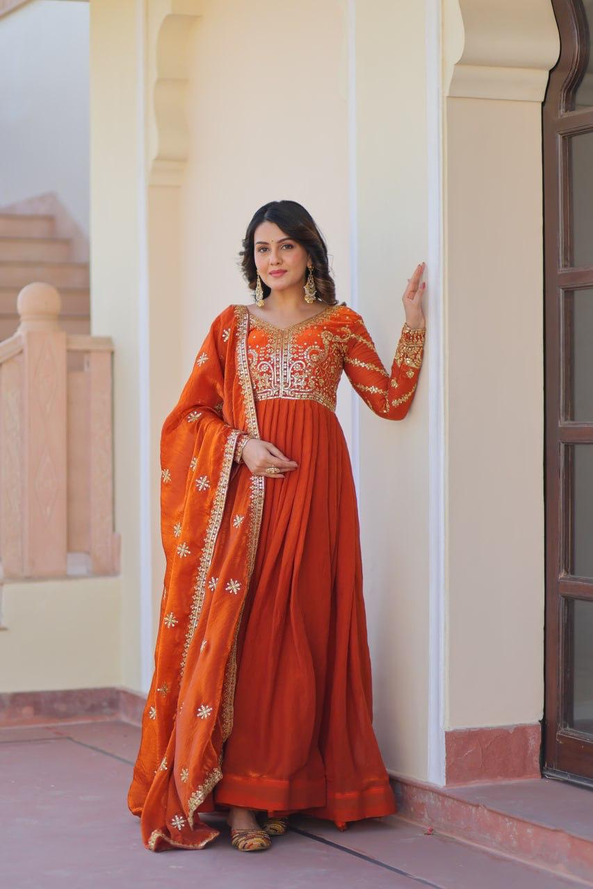 Woman in an orange traditional outfit standing against a beige wall.