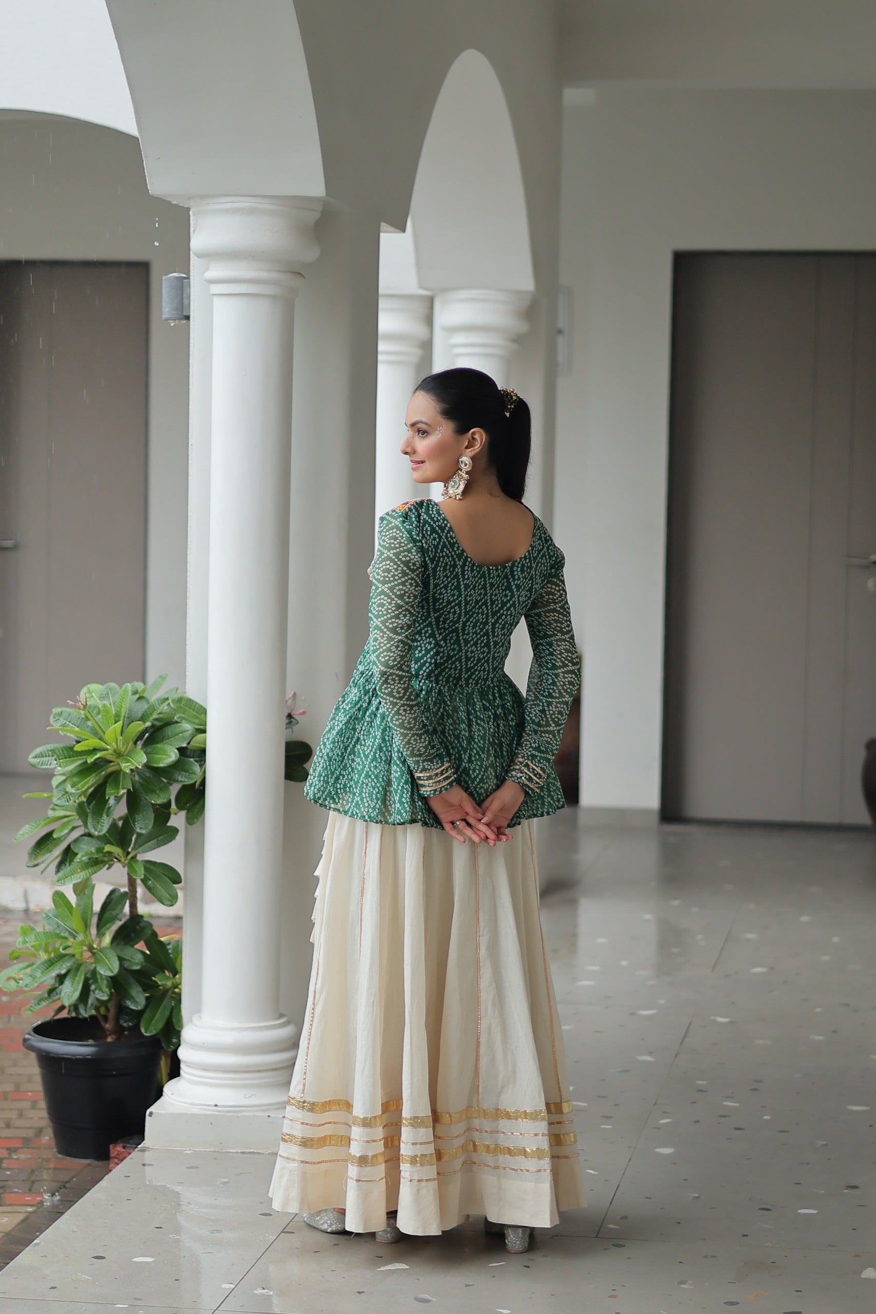 Woman in a green top and white skirt standing in a hallway with columns.
