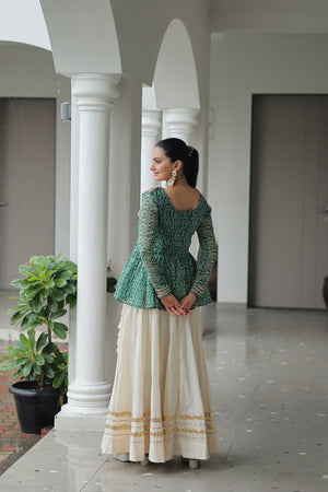 Woman in a green top and white skirt standing in a hallway with columns.