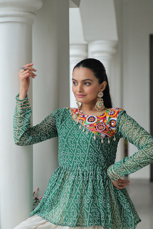 Woman wearing a green patterned dress with colorful embroidery, standing against white columns.