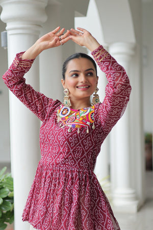 Woman in a red patterned dress with colorful embellishments posing outdoors.
