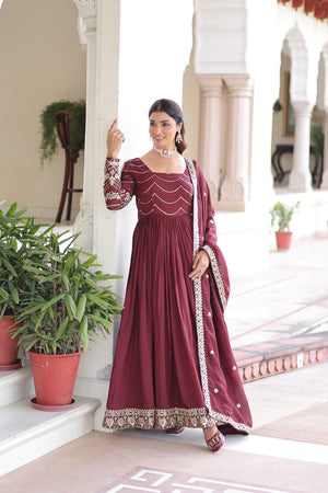 Woman in a maroon traditional outfit standing in an elegant indoor setting with plants.
