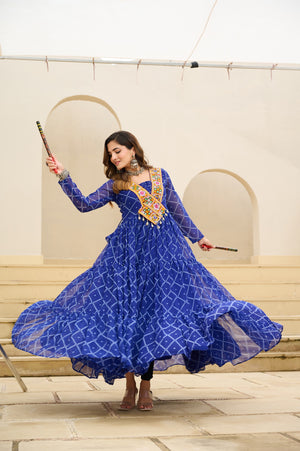 Woman in a blue dress with floral patterns holding sticks in an indoor setting