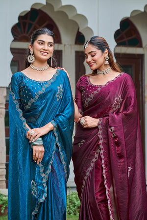 Two women in traditional sarees standing in front of an architectural background