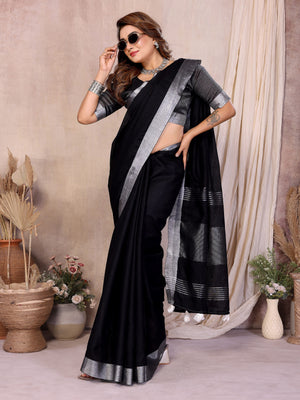 Woman wearing a black saree with silver border in a decorated room.