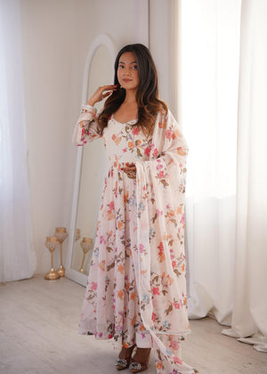 Woman wearing a floral dress standing in a softly lit room with white curtains.