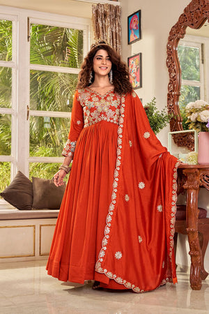 Woman in a red traditional outfit with floral patterns standing in a room with a window and decor.