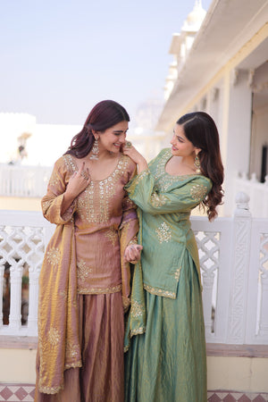 Two women in traditional outfits standing on a balcony with a building in the background.