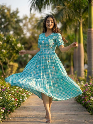 Woman in a blue dress with floral pattern standing on a pathway surrounded by greenery.