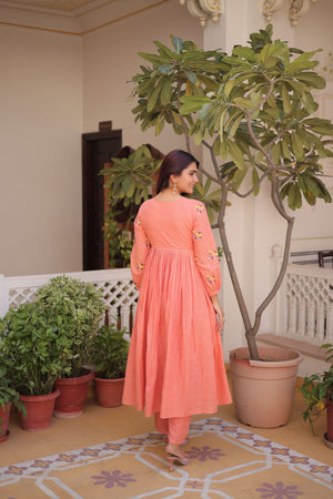 Woman in a peach-colored dress standing in a room with plants and decorative tiles.