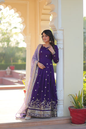 Woman in a purple traditional outfit standing in front of a decorative wall.