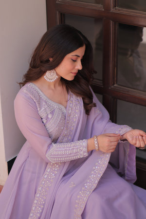 Woman in a lavender traditional outfit with intricate designs, sitting indoors.