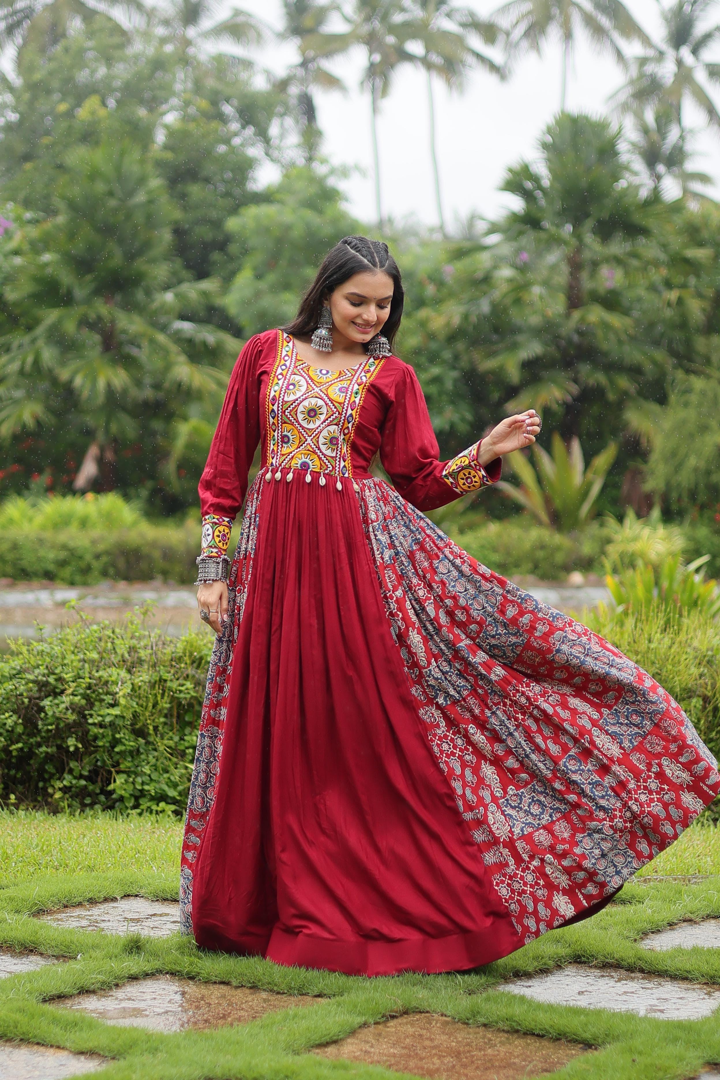 Woman in a red traditional outfit with floral patterns standing outdoors in a garden.