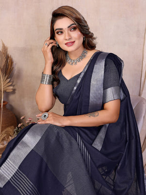 Woman wearing a dark blue saree with silver stripes, sitting against a neutral background.