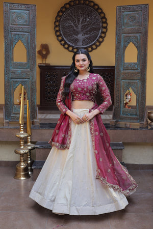 Woman in a traditional magenta and white outfit standing in a decorated room with wooden panels and a tree emblem.