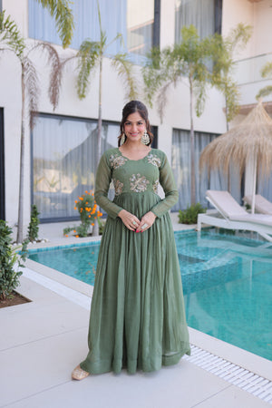 Woman in a green dress standing by a pool with a modern building and plants in the background