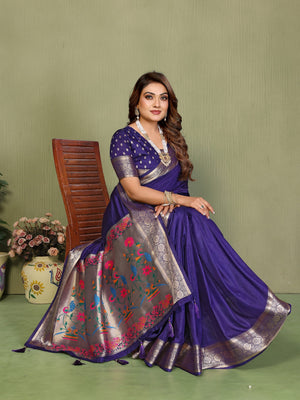 Woman in a traditional purple saree with floral patterns sitting on a chair against a green background.