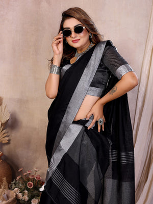Woman wearing a black saree with silver border against a beige background