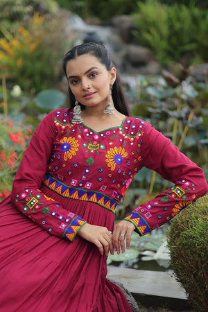 Woman in a vibrant traditional outfit with colorful embroidery, standing in a garden setting.