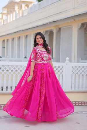 Woman in a bright pink traditional outfit with white embroidery standing in front of a white architectural background.