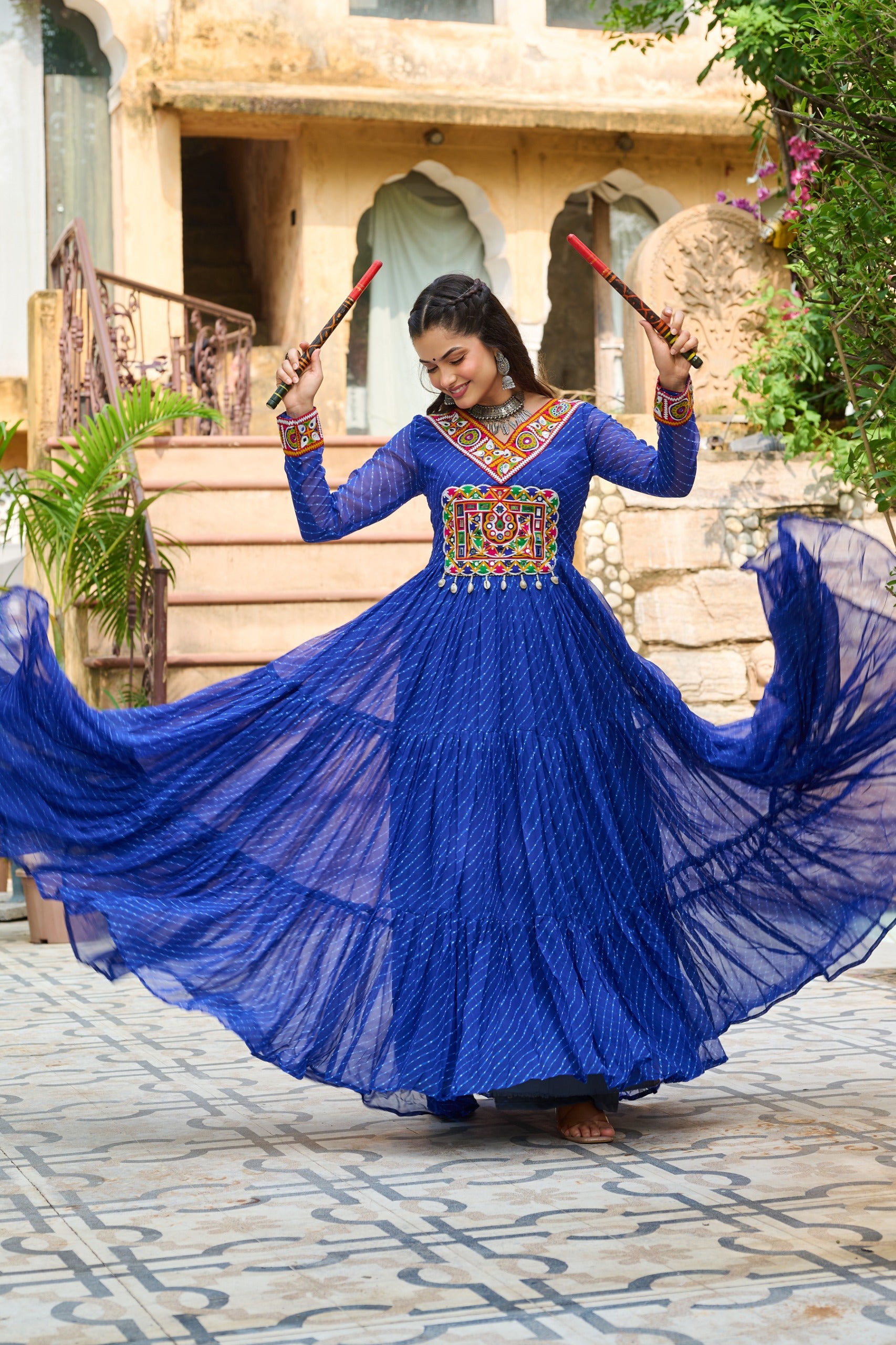 Woman in a blue traditional outfit with colorful embroidery, dancing outdoors.