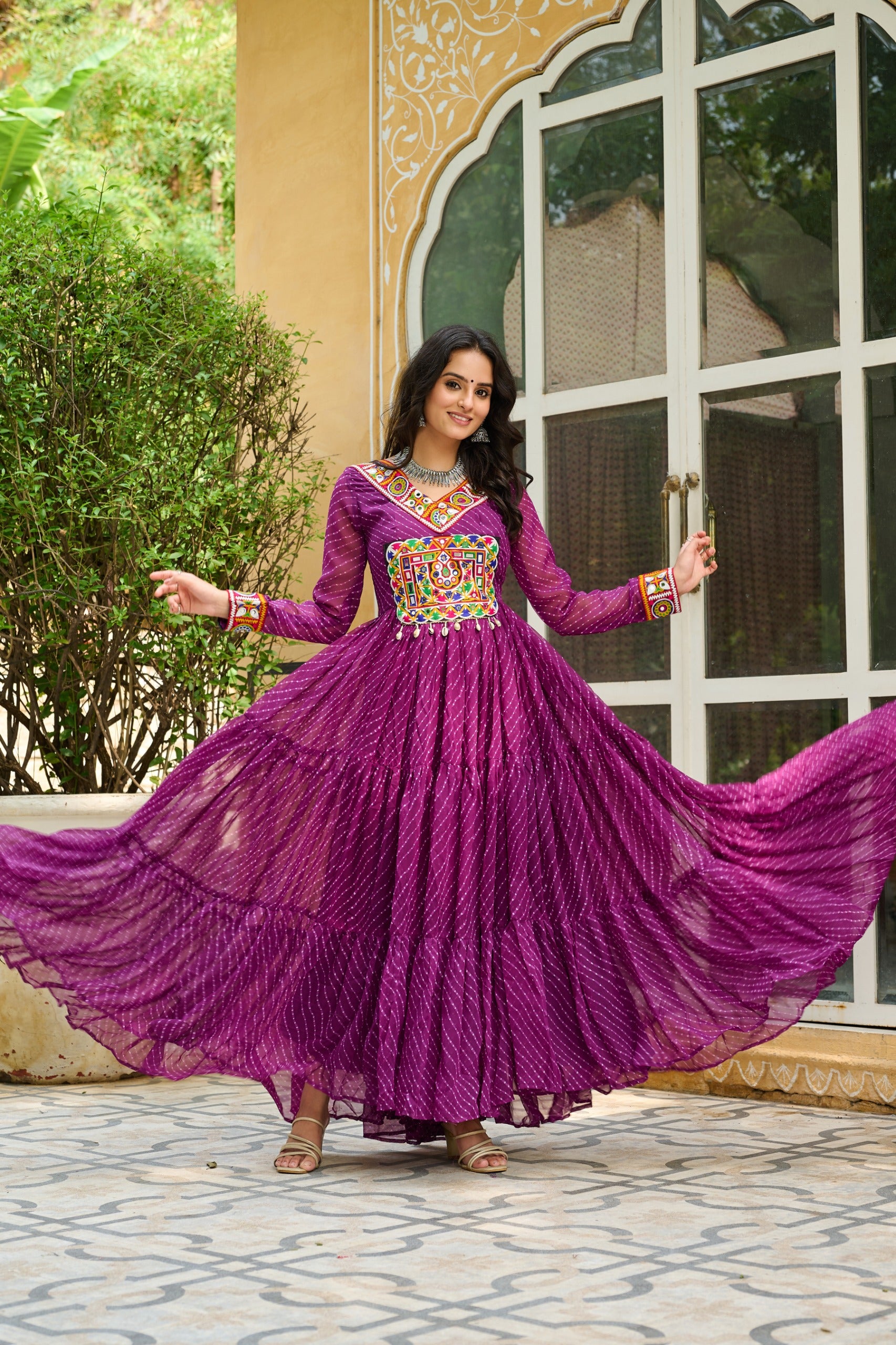 Woman in a purple traditional dress with floral patterns standing outdoors.
