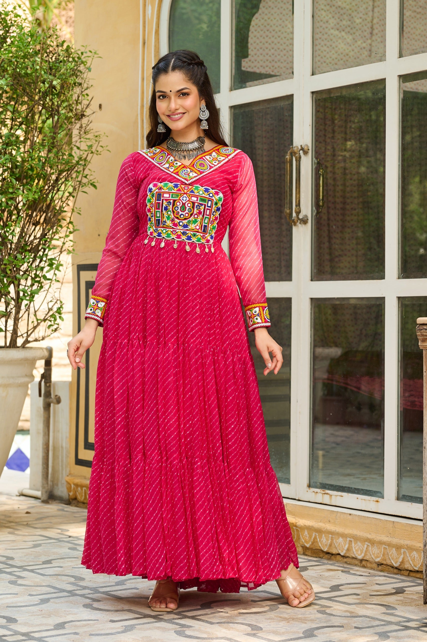 Woman wearing a vibrant pink traditional outfit with colorful embroidery in an outdoor setting.