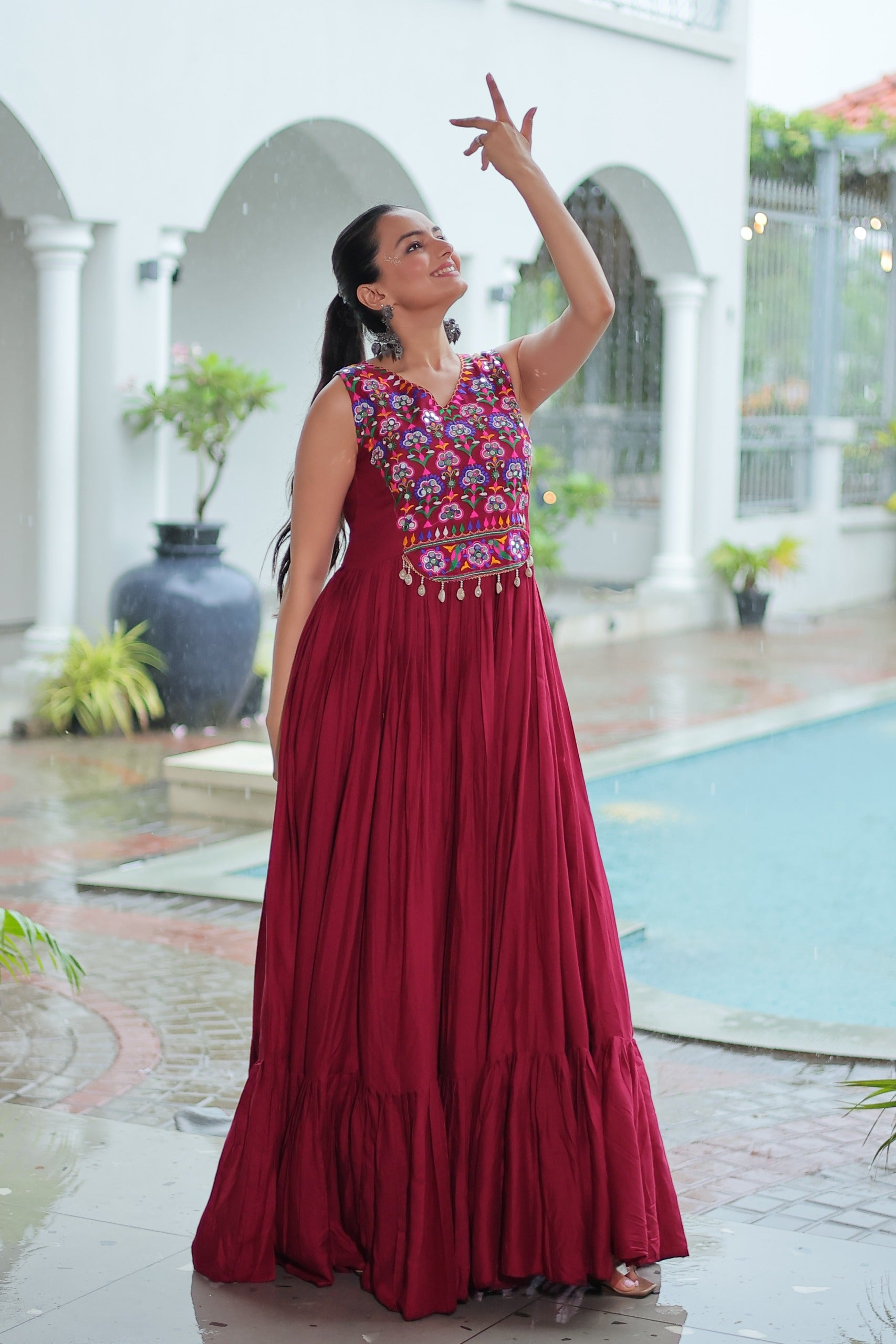 Woman in a red dress with floral top standing by a poolside.