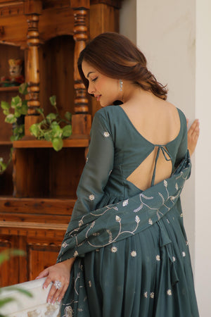 Woman in a green dress with floral patterns standing indoors.