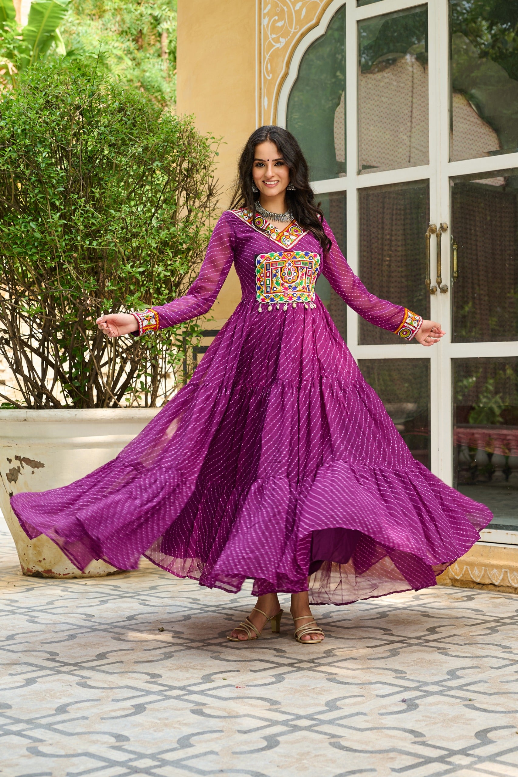 Woman in a purple traditional outfit with colorful embellishments outdoors.