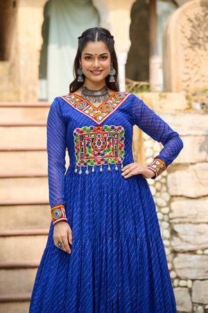 Woman wearing a blue traditional outfit with colorful embroidery in an outdoor setting.