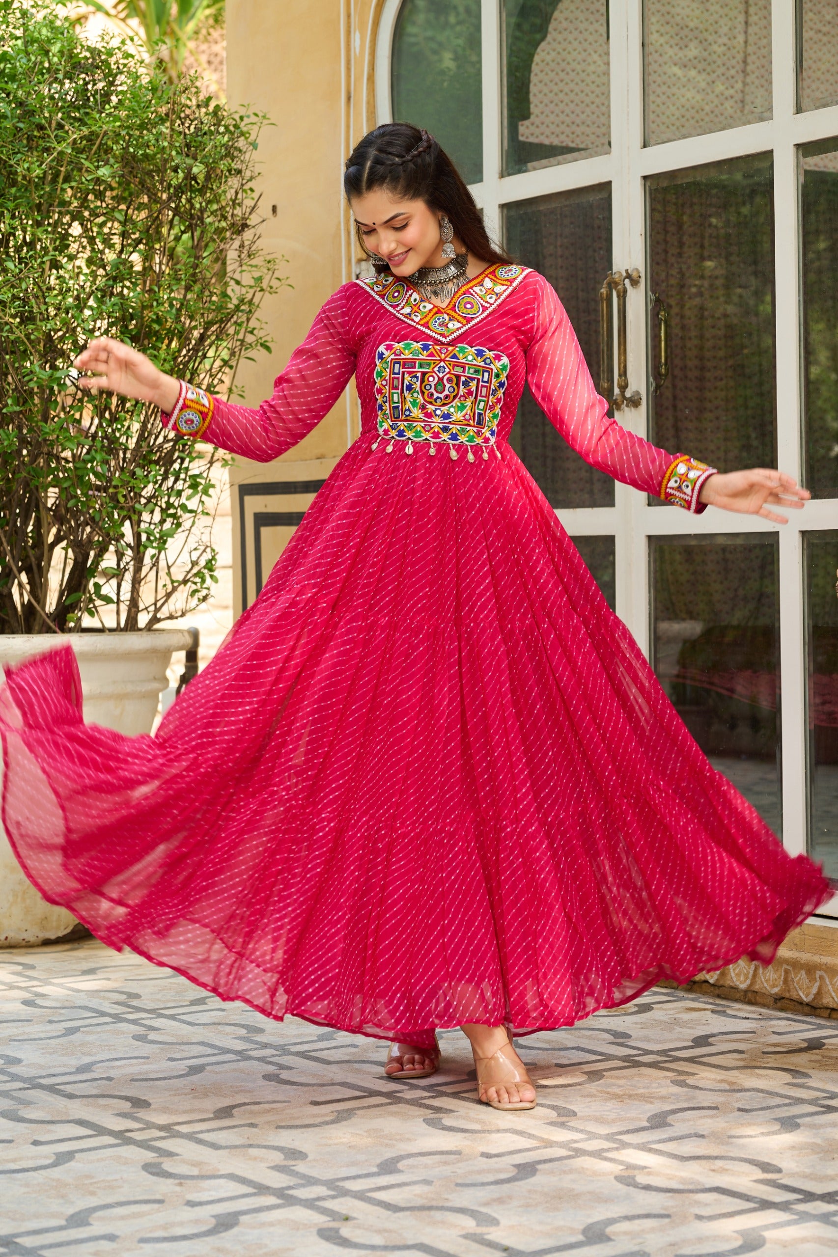 Woman in a bright pink traditional outfit with colorful embroidery, standing outdoors.