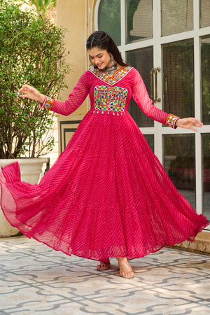 Woman in a bright pink traditional outfit with colorful embroidery, standing outdoors.