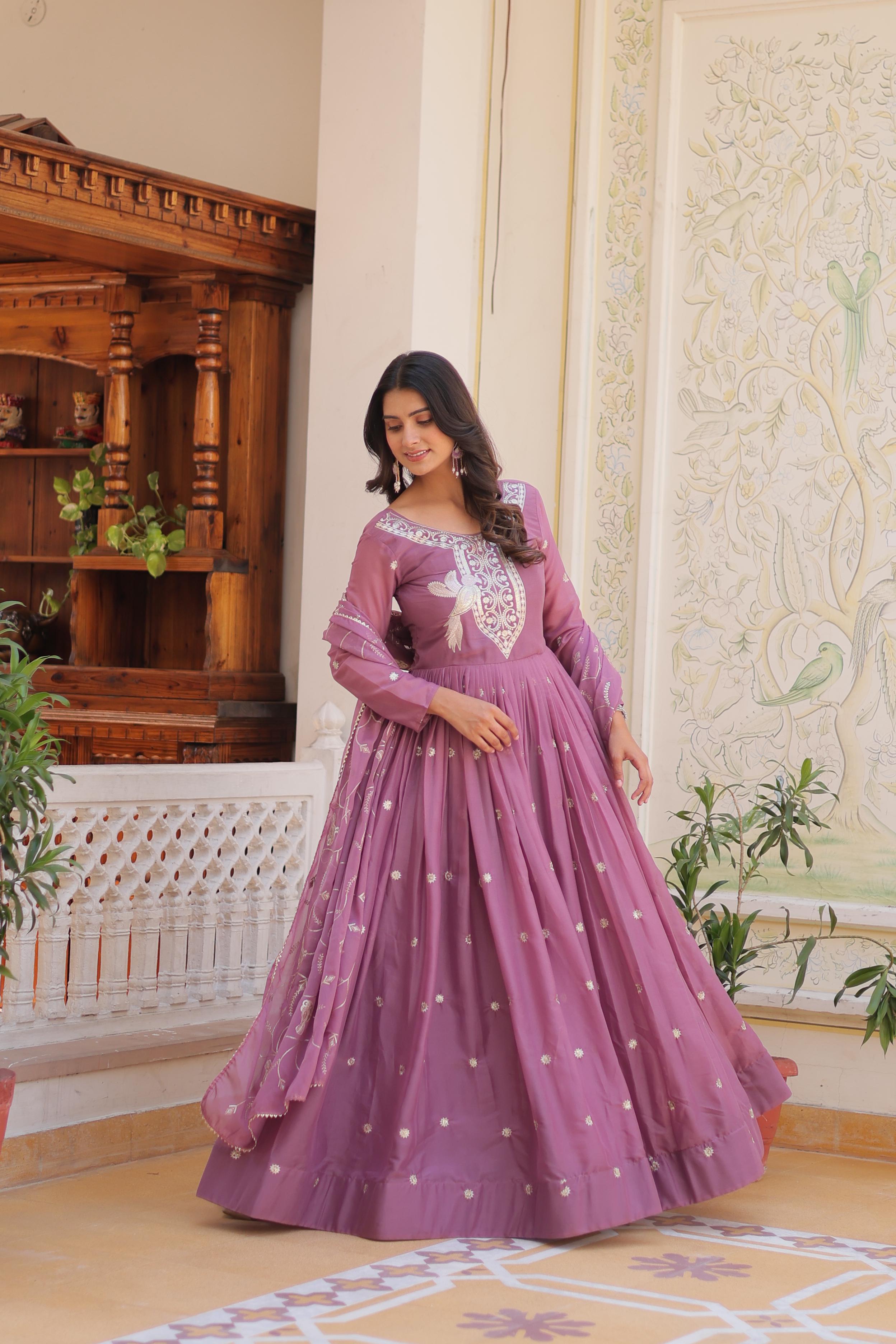Woman in a purple gown with white embroidery standing in an elegant room.