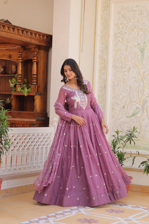 Woman in a purple gown with white embroidery standing in an elegant room.