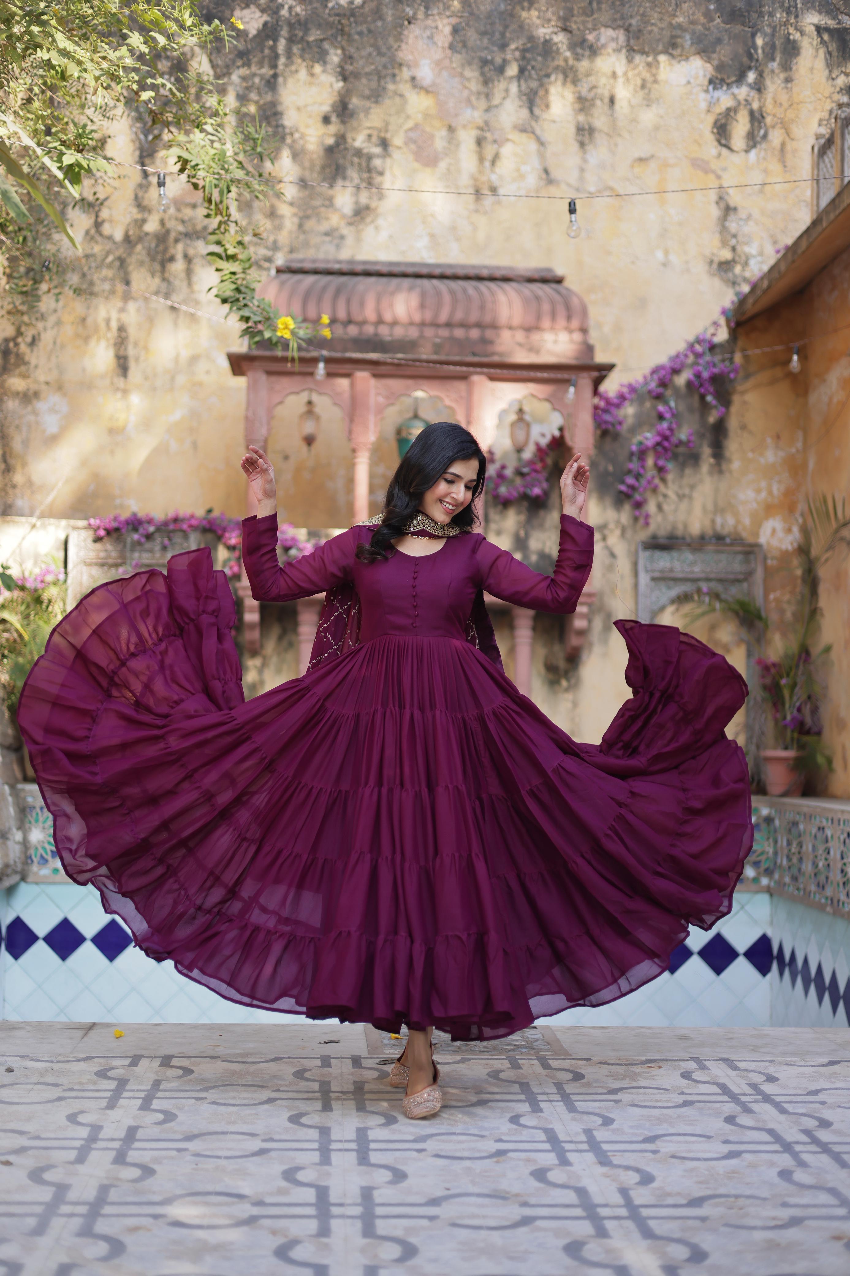 Woman in a purple dress dancing in an outdoor setting with a textured wall and decorative elements.