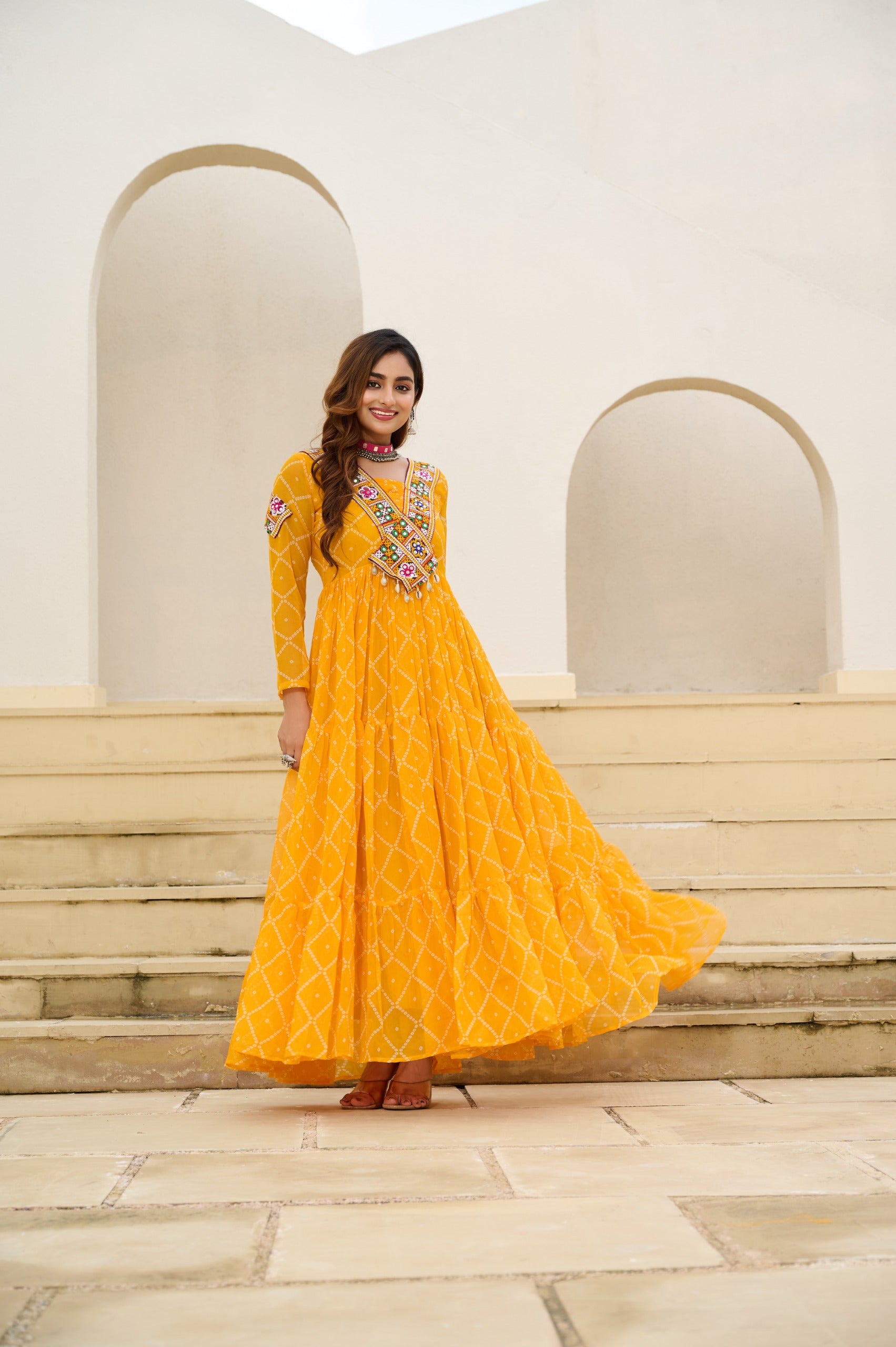 Woman in a yellow traditional outfit standing on steps with a white architectural background