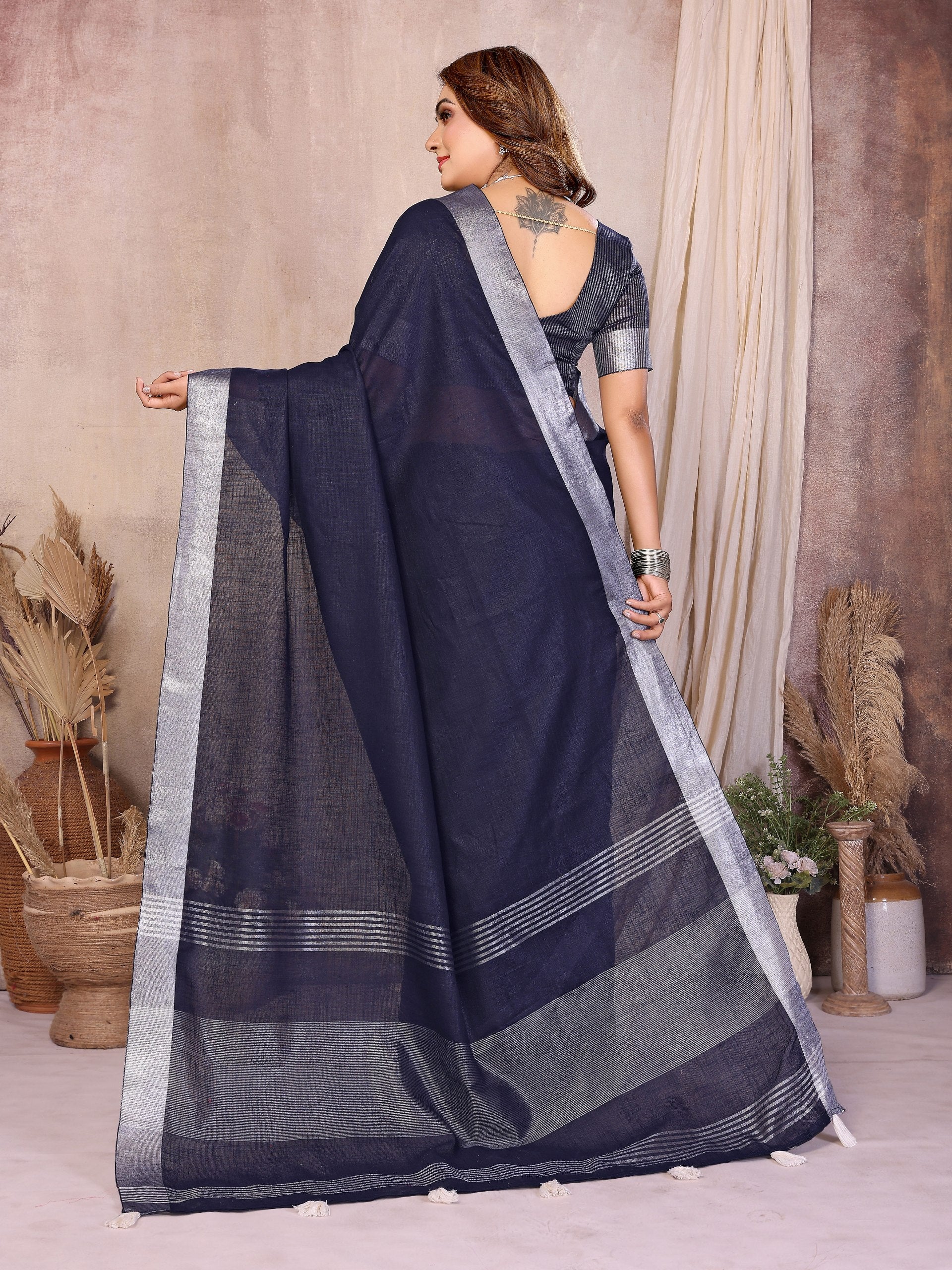Woman wearing a dark blue saree with a light border, standing against a neutral background.