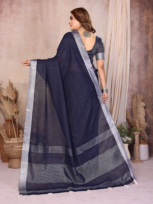 Woman wearing a dark blue saree with a light border, standing against a neutral background.