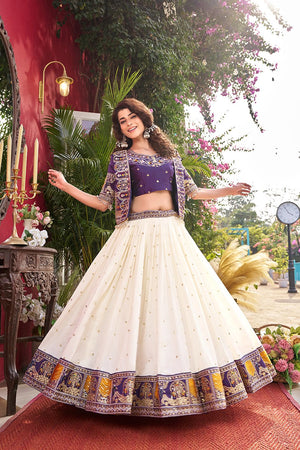 Woman in traditional outfit with white skirt and purple top, standing outdoors.
