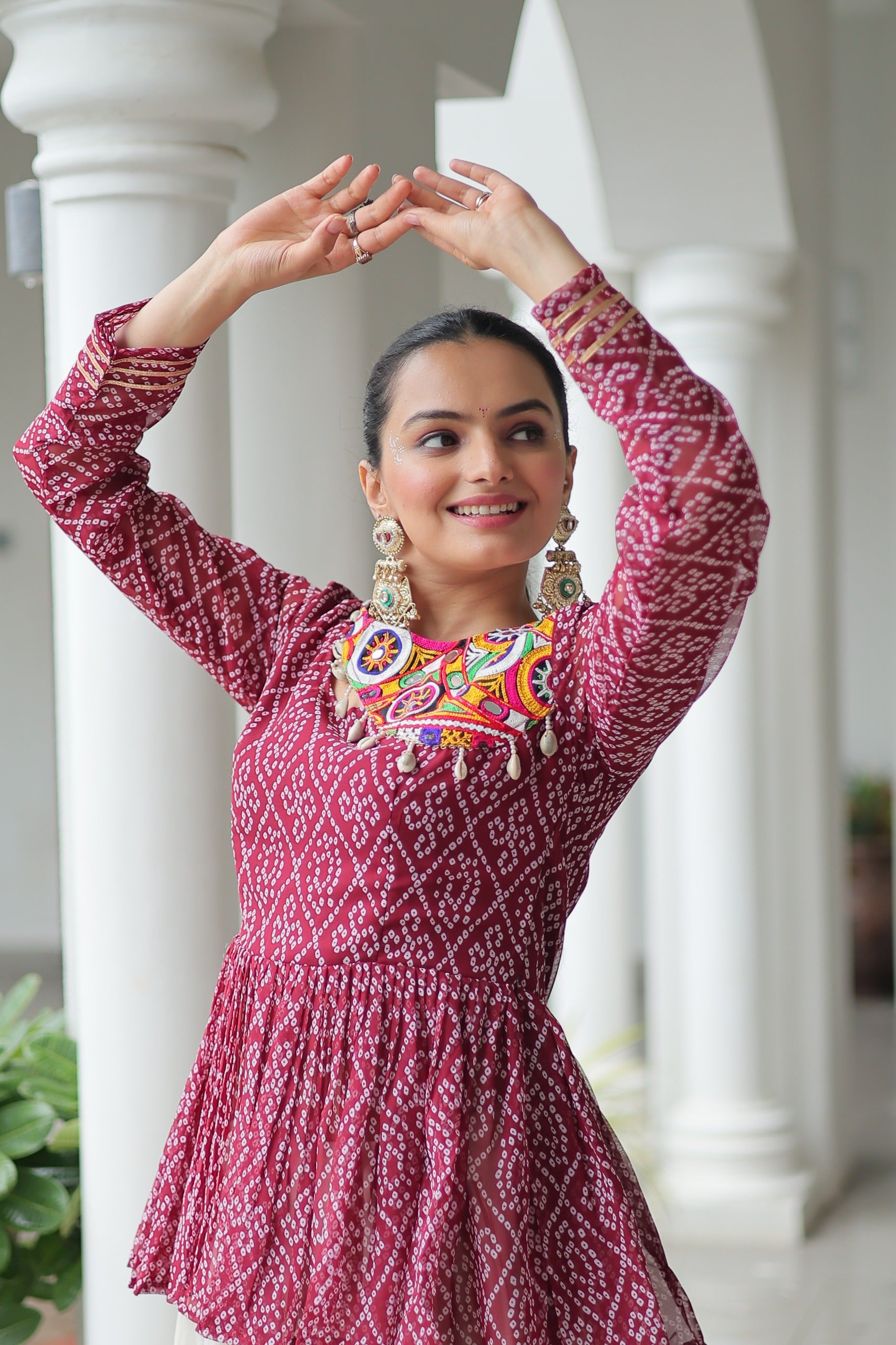 Woman in a red patterned dress with colorful embellishments posing outdoors.