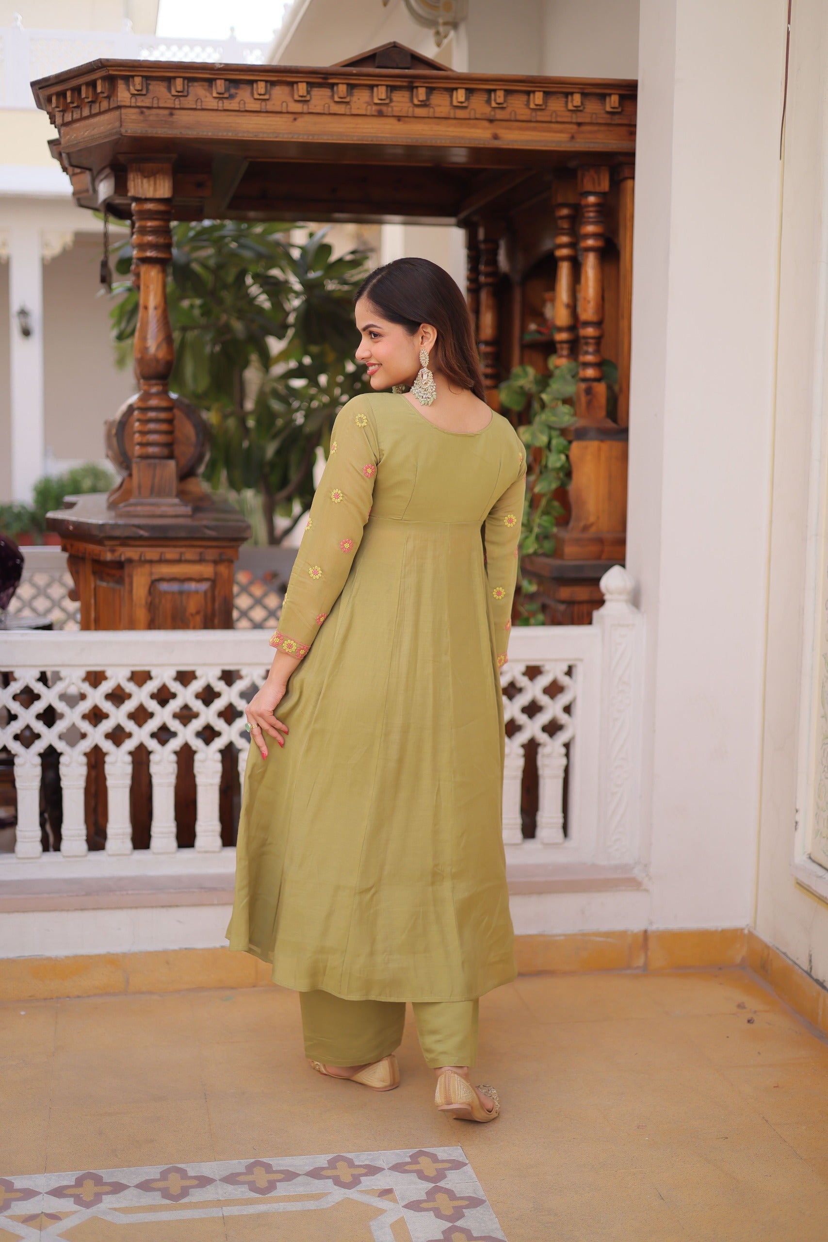 Woman in a green traditional outfit standing in a decorated indoor setting.