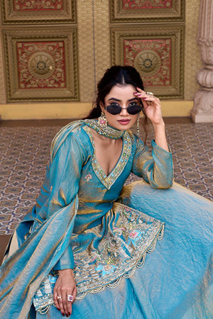 Woman in a blue traditional outfit with intricate designs, sitting on a patterned floor.