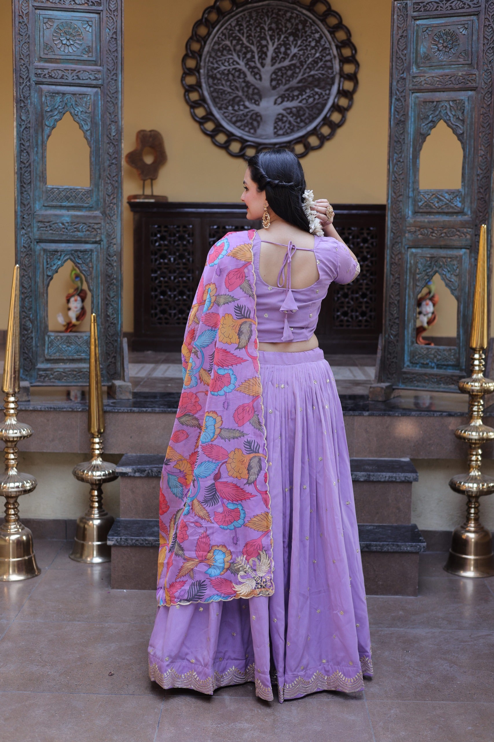 Woman in a lavender traditional outfit with a colorful shawl in a decorated room.