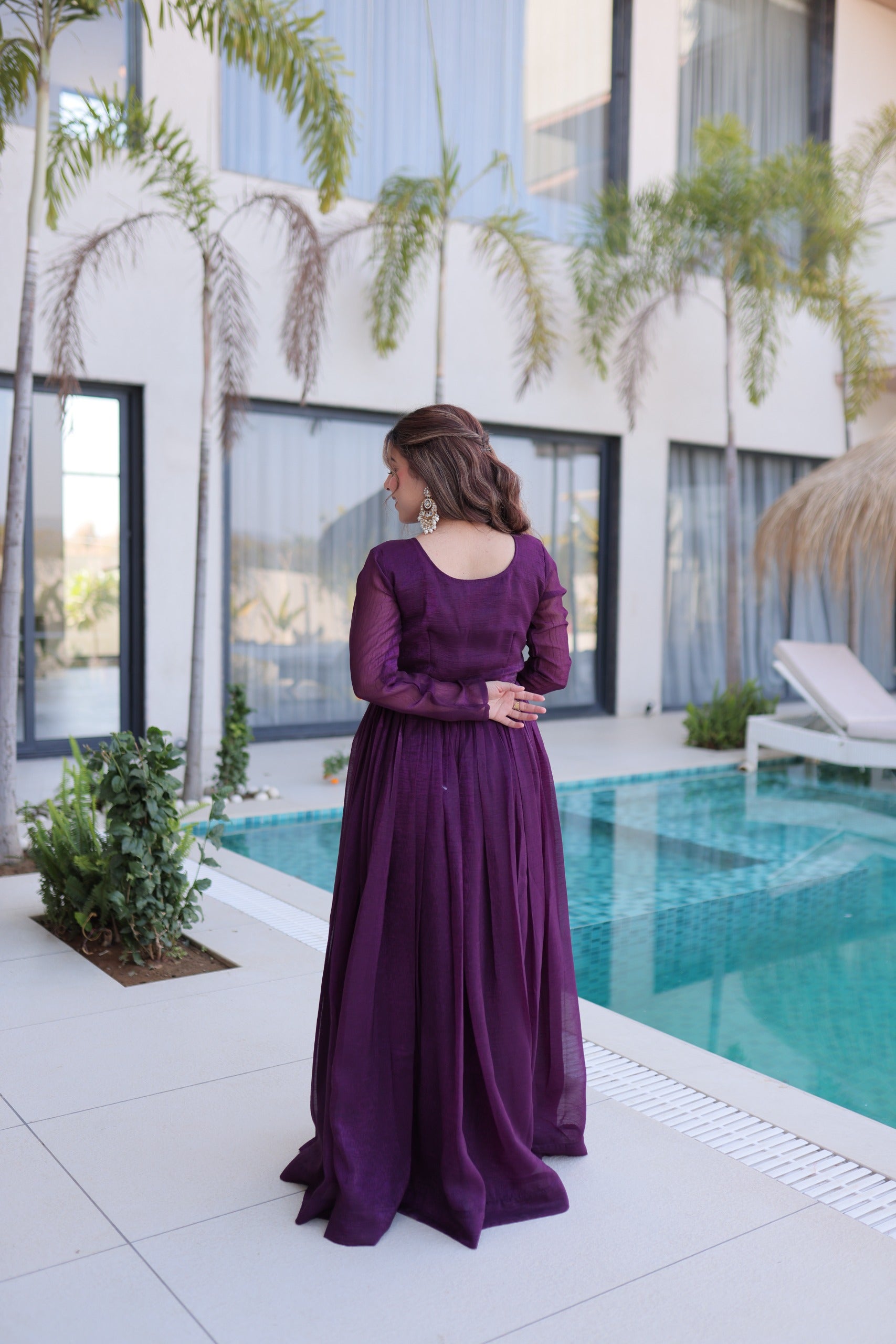 Woman in a purple dress standing by a pool with a modern building and plants in the background