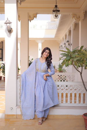 Woman in a light blue traditional outfit standing on a balcony with decorative elements.