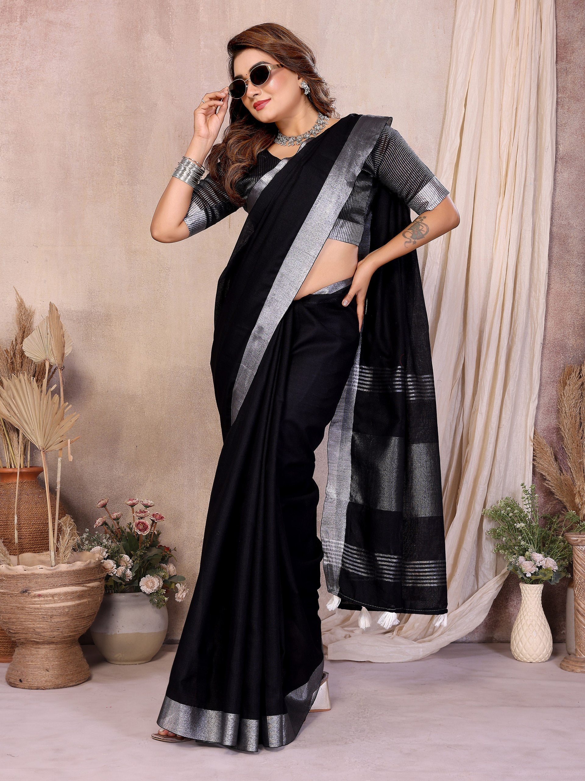 Woman wearing a black saree with silver border in a decorated room.