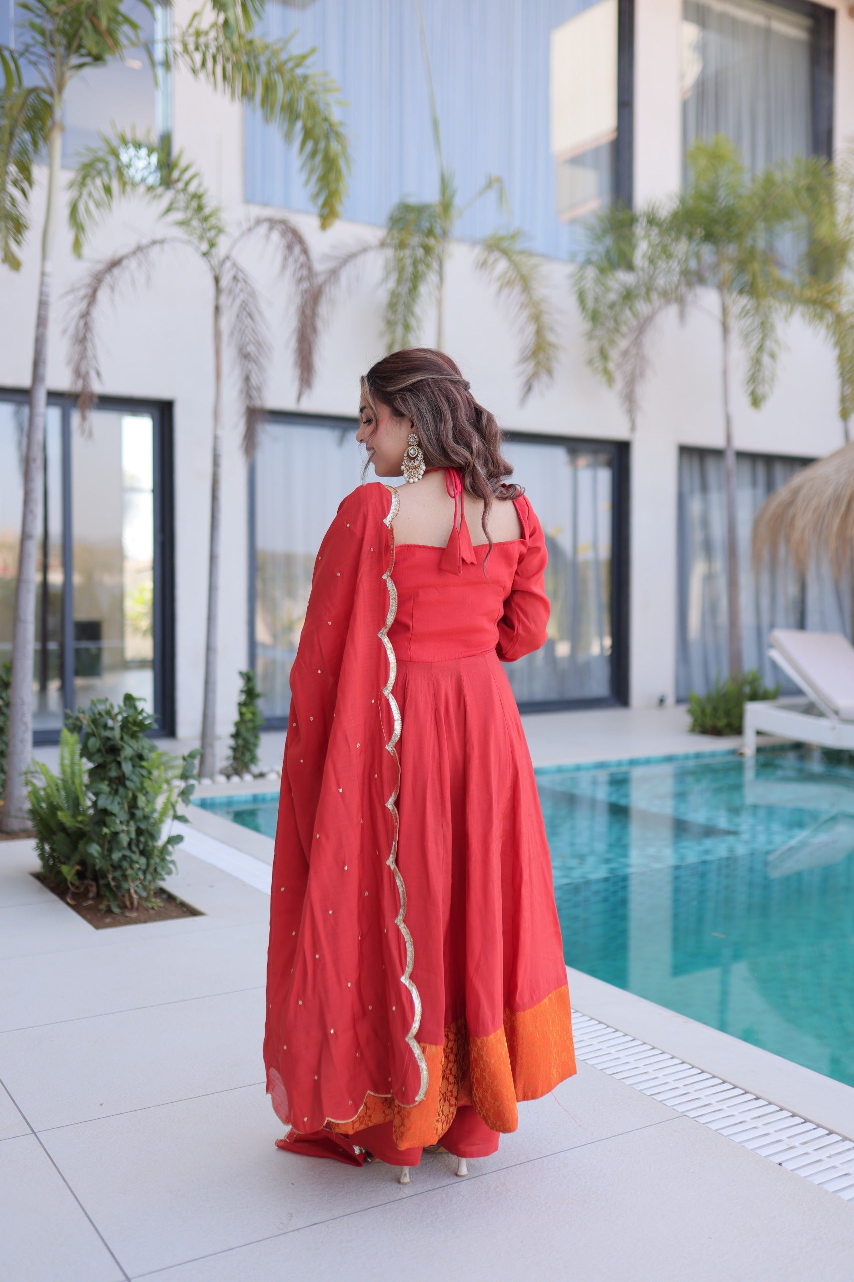 Woman in a red traditional outfit standing by a pool with a modern building in the background