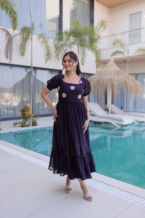Woman in a dark purple dress standing by a pool with a modern building and plants in the background