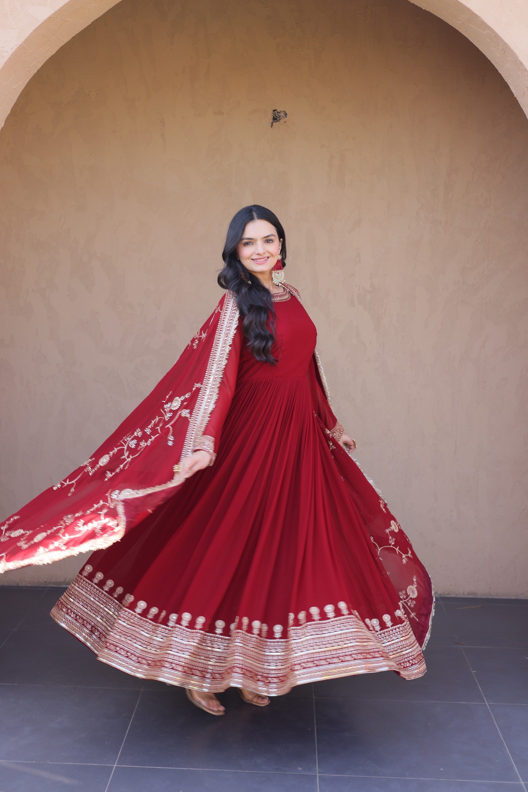Woman in a red traditional outfit with white embroidery standing against a beige wall.